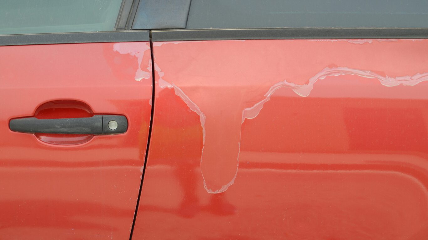 Peeling paint on the side of a red car.