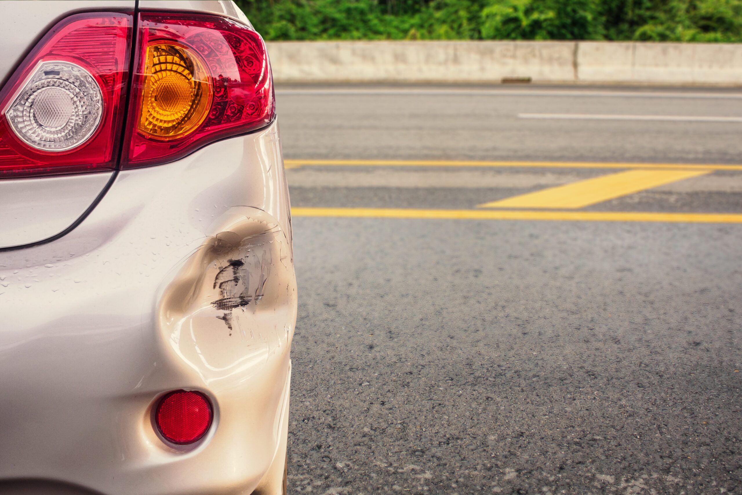 Close-up of a dented and scratched rear bumper on a car.