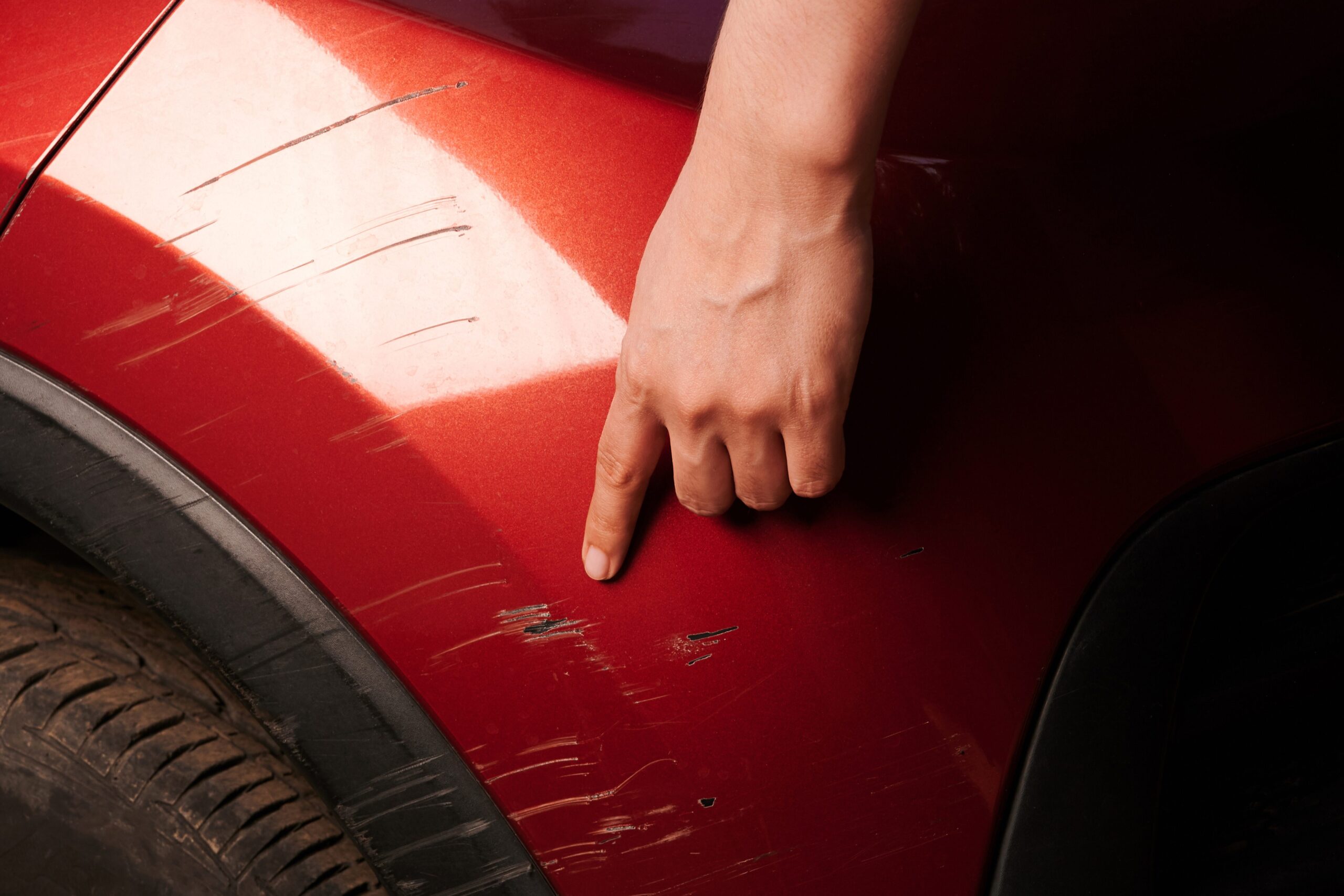 A technician inspecting scratches of a red car to assess panel damage.