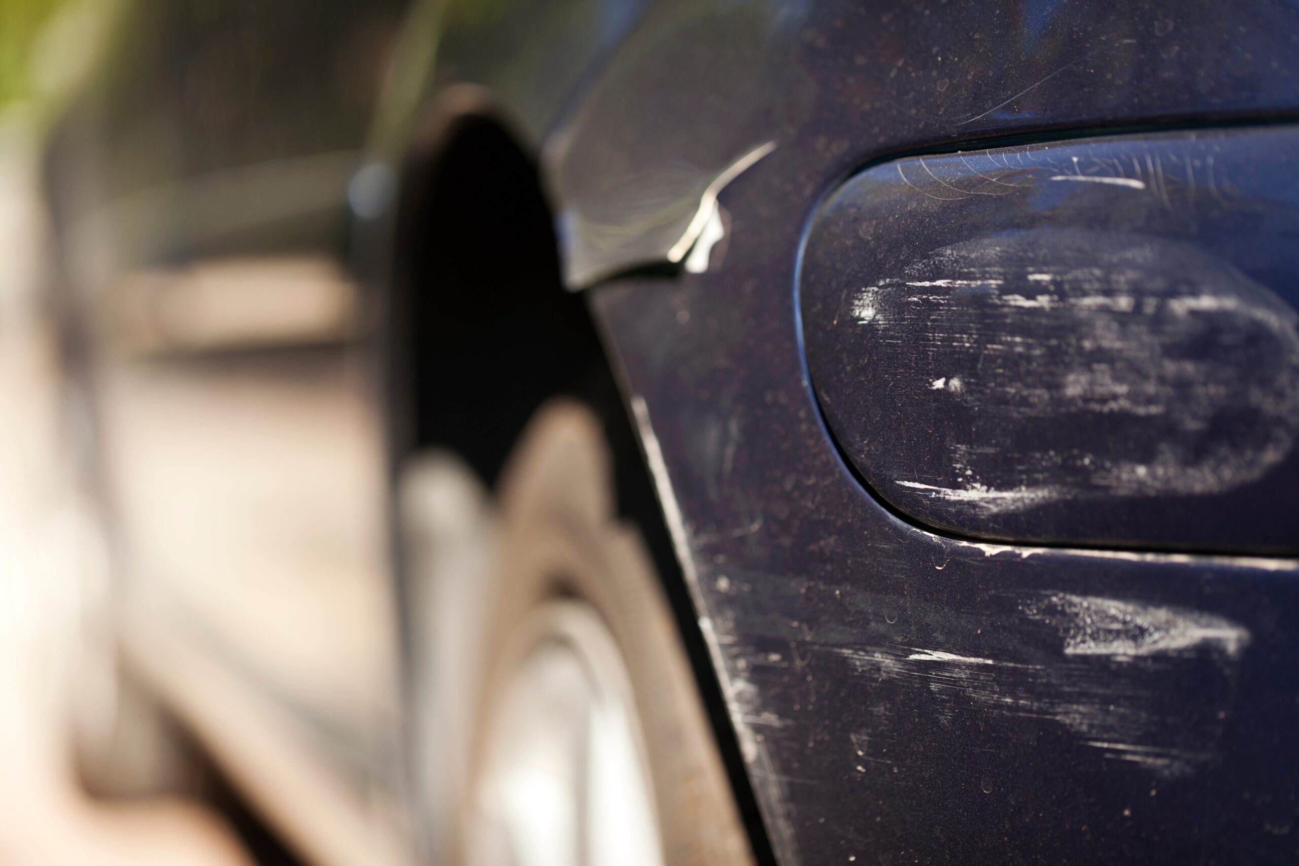 Car scratch repairs needed on a dark blue car’s front panel scratched by a gate in a driveway.