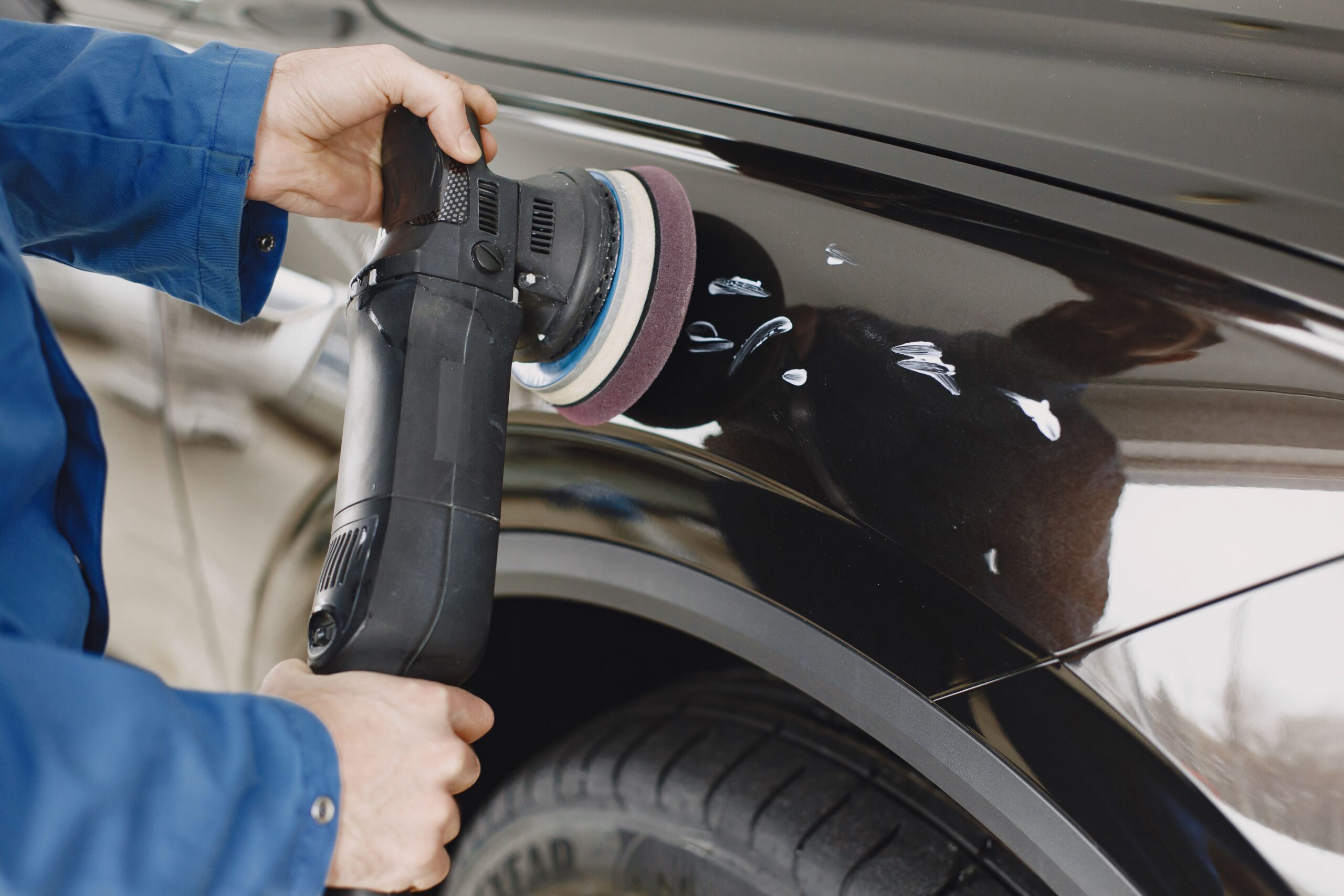 Technician polishing a black car panel during paint repair after a minor accident.